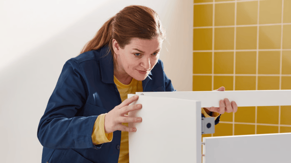Zaměstnankyně IKEA, která montuje novou bílou umyvadlovou skříňku do koupleny.