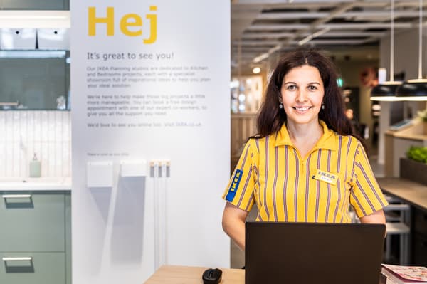Zaměstnankyně IKEA ve žluté košili stojí za stolem s notebookem a je připravena pomoci zákazníkům.