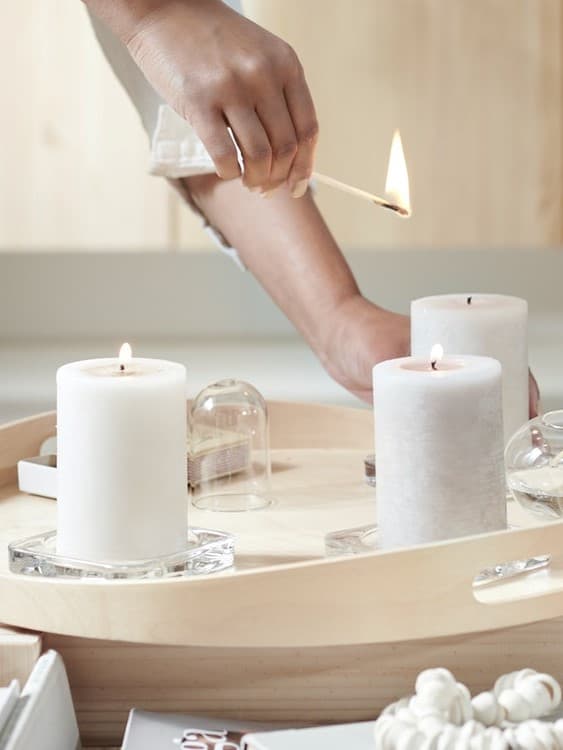 Zapaľovanie bielej sviečky na drevenom podnose s ďalšími sviečkami – elegantná dekorácia IKEA pre útulný domov.