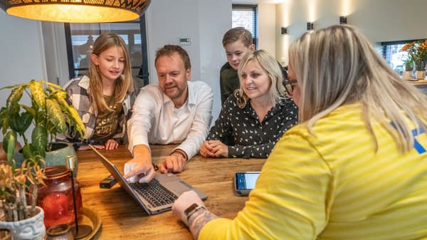 Zaposlena podjetja IKEA v rumeni majici sedi za prenosnim računalnikom in prikazuje načrte na domu, uporabne za načrtovanje kuhinje.