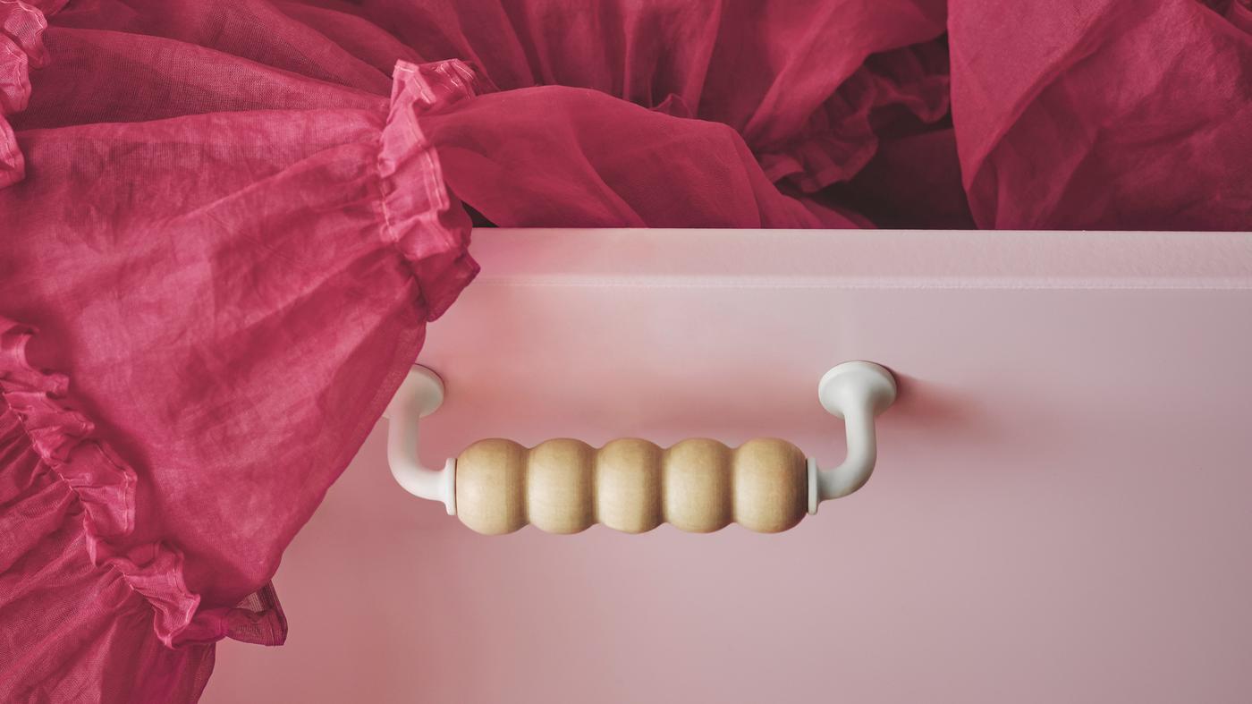 Zásuvkový diel SMÅSTAD s jedinečnou drevenou rukoväťou upevnenou na čele svetloružovej zásuvky s vyčnievajúcou sukňou z tylu.