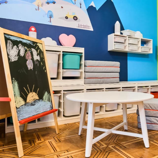 Zdjęcie pokoju dziecięcego z tablica do malowania, białym okrąfłym stolikiem i systeme do przechowywyania TROFAST