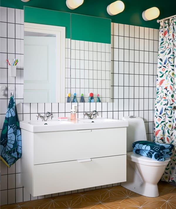 Zelená kúpeľňa s bielym obkladom a veľkým zrkadlom a skrinkou IKEA GODMORGON/ODENSVIK s dvomi umývadlami s dvomi zásuvkami.