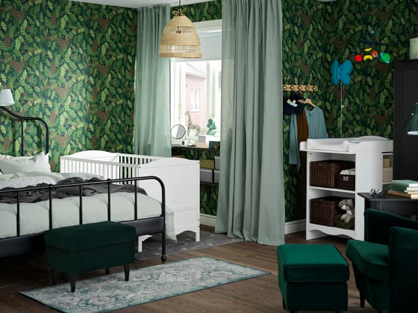 Zelena spavaća soba/dečja soba sa stolom za povijanje i krevecem u beloj boji, crnim krevetnim okvirom i belim/zelenim zavesama.
