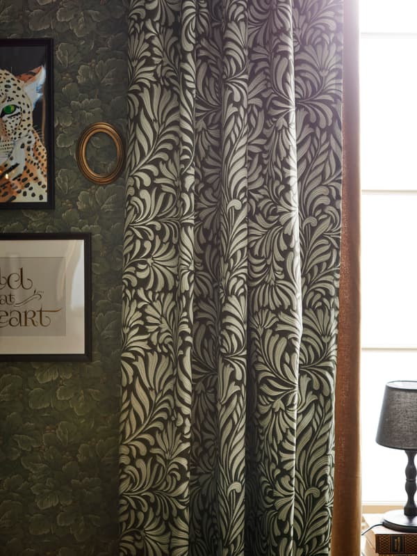 Zelené vzorované závesy TRÅGSPINNARE vedľa steny so zelenými tapetami s prírodnými motívmi.