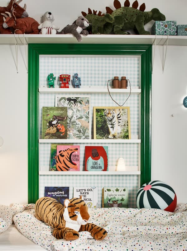 Zeleni i bijeli zid iznad kreveta u dječjoj sobi. Plišane igračke na zidnoj polici i knjige na MOSSLANDA letvama za slike.