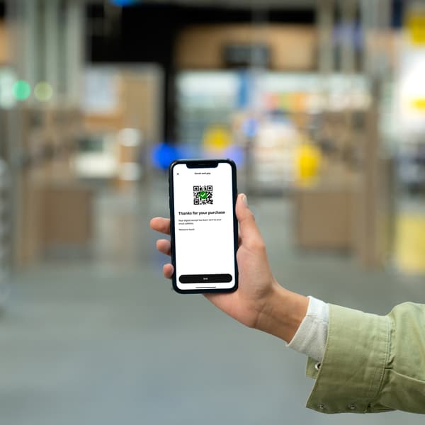 Žena drži telefon u robnoj kući IKEA na kojem je otvorena IKEA aplikacija i opcija IKEA Scan.