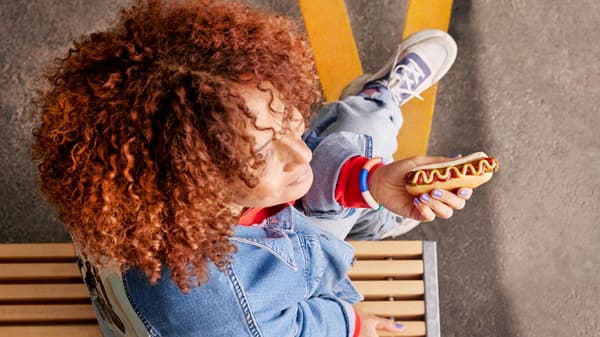 Žena, která sedí na lavičce a jí bezmasý hotdog.