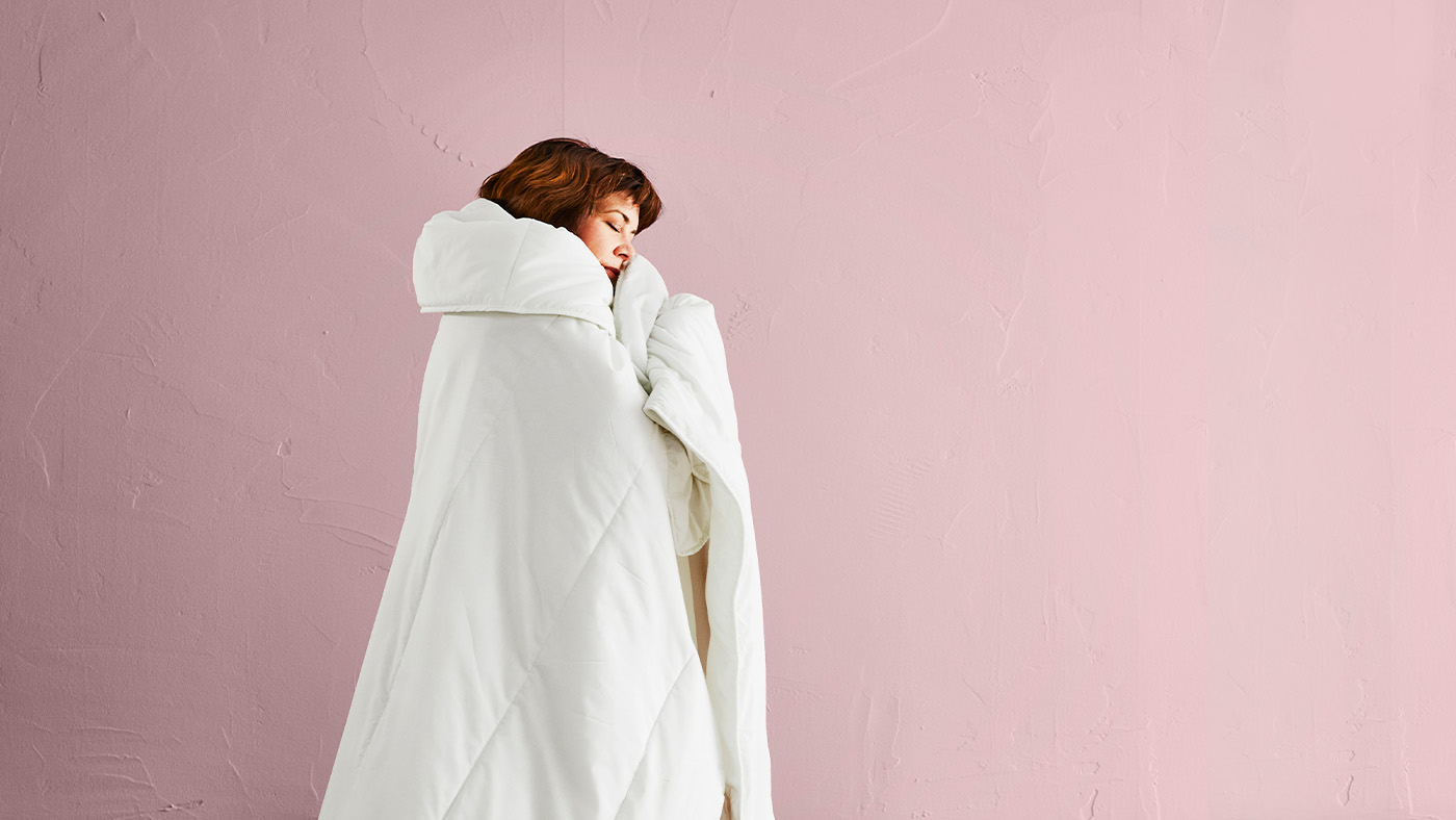 Žena oblečená v peřině stojící před růžovou stěnou