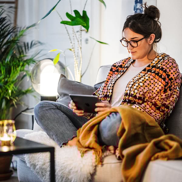 Žena sedící na pohovce m v ruku knihu a čte si.