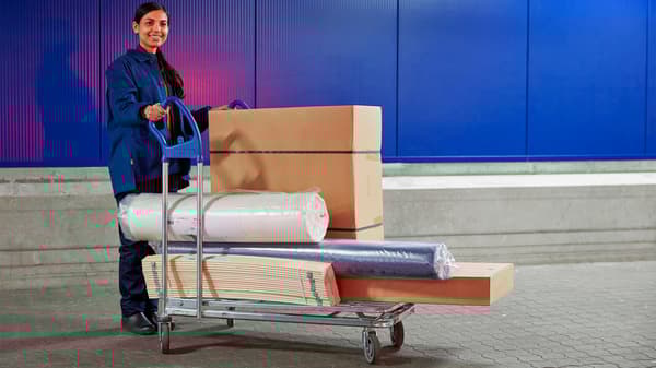 Žena tlačí pred sebou vozík naložený zabaleným tovarom IKEA.