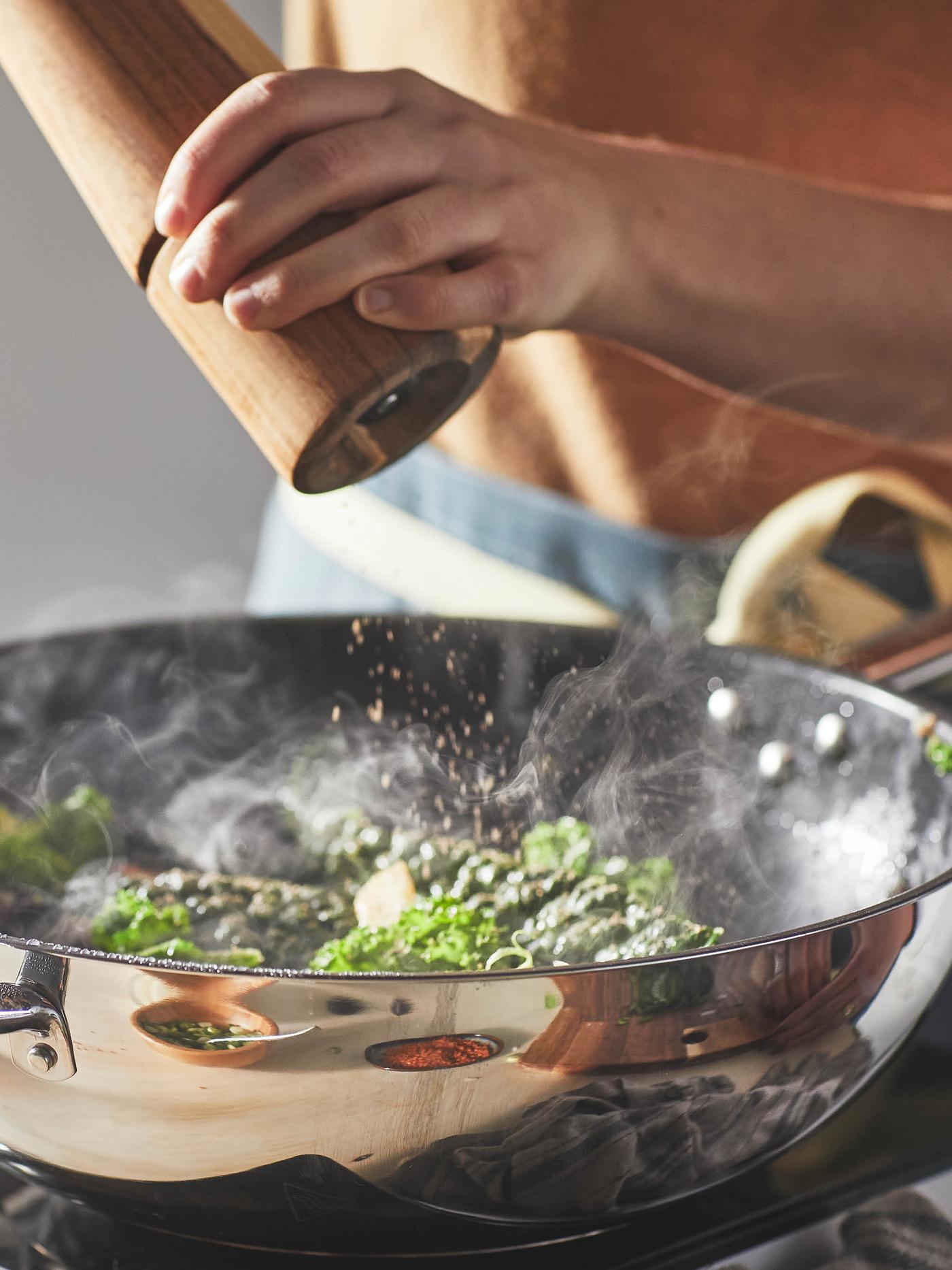 Žena v béžovém svetru koření zeleninu v pánvi wok IKEA 365+.