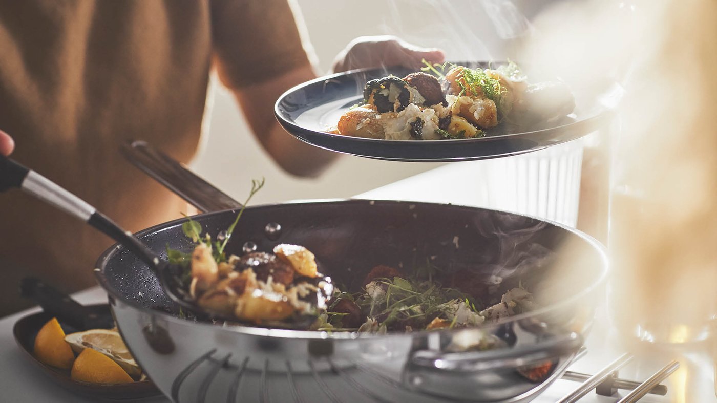 Žena v béžovom svetri naberá z panvice wok IKEA 365+ na tanier zmes guľôčok a zeleniny.