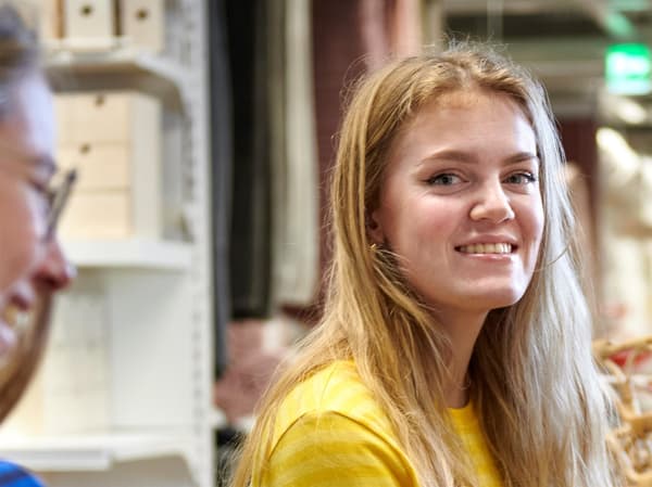 Žena v uniforme IKEA sa s úsmevom pozerá do fotoaparátu.