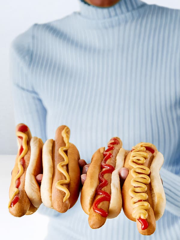 Žena ve světle modrém svetru se čtyřmi hotdogy