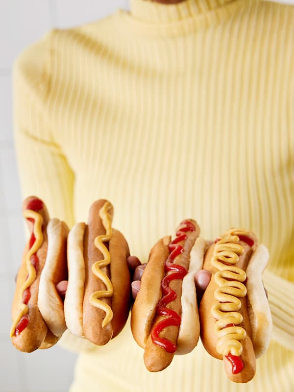Žena ve světle žlutém svetru se čtyřmi hotdogy