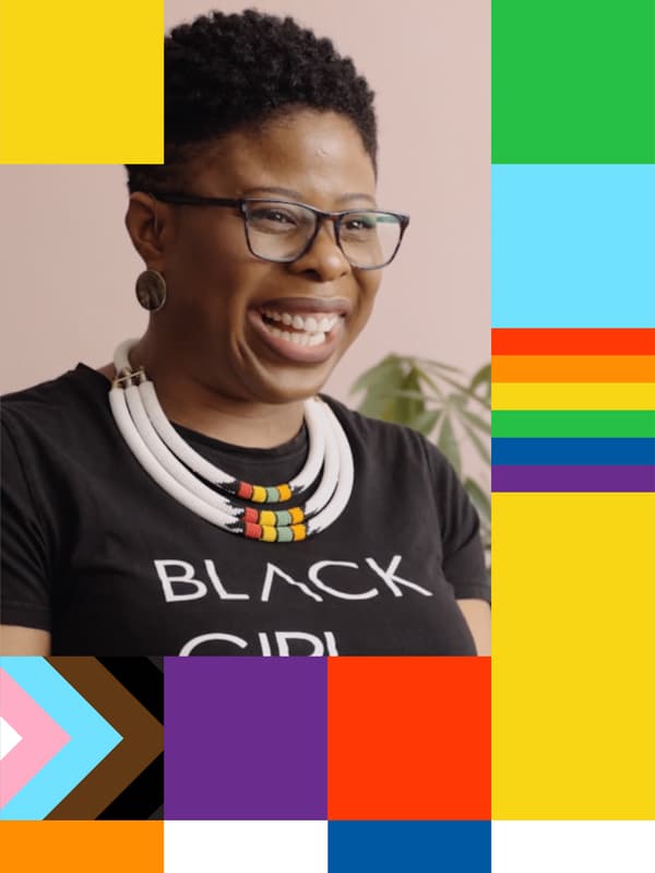 Žena z komunity LGBT + v tričku s nápisem „Black girl magic“ sedí v bytě a směje se.
