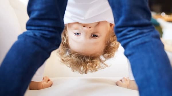 Zēns, kurš spēlējas, stāv uz visām četrām uz balta dīvāna
