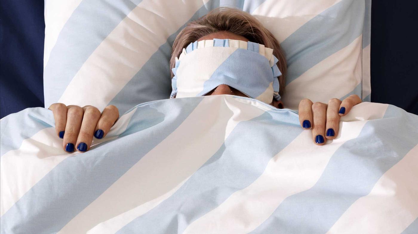 Ženska s spalnimi očali v postelji z belo-modri črtasto posteljnino.