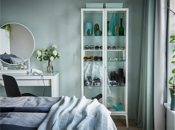 Zielona ściana sypialni ze szklaną szafką i białą toaletką z lustrem.