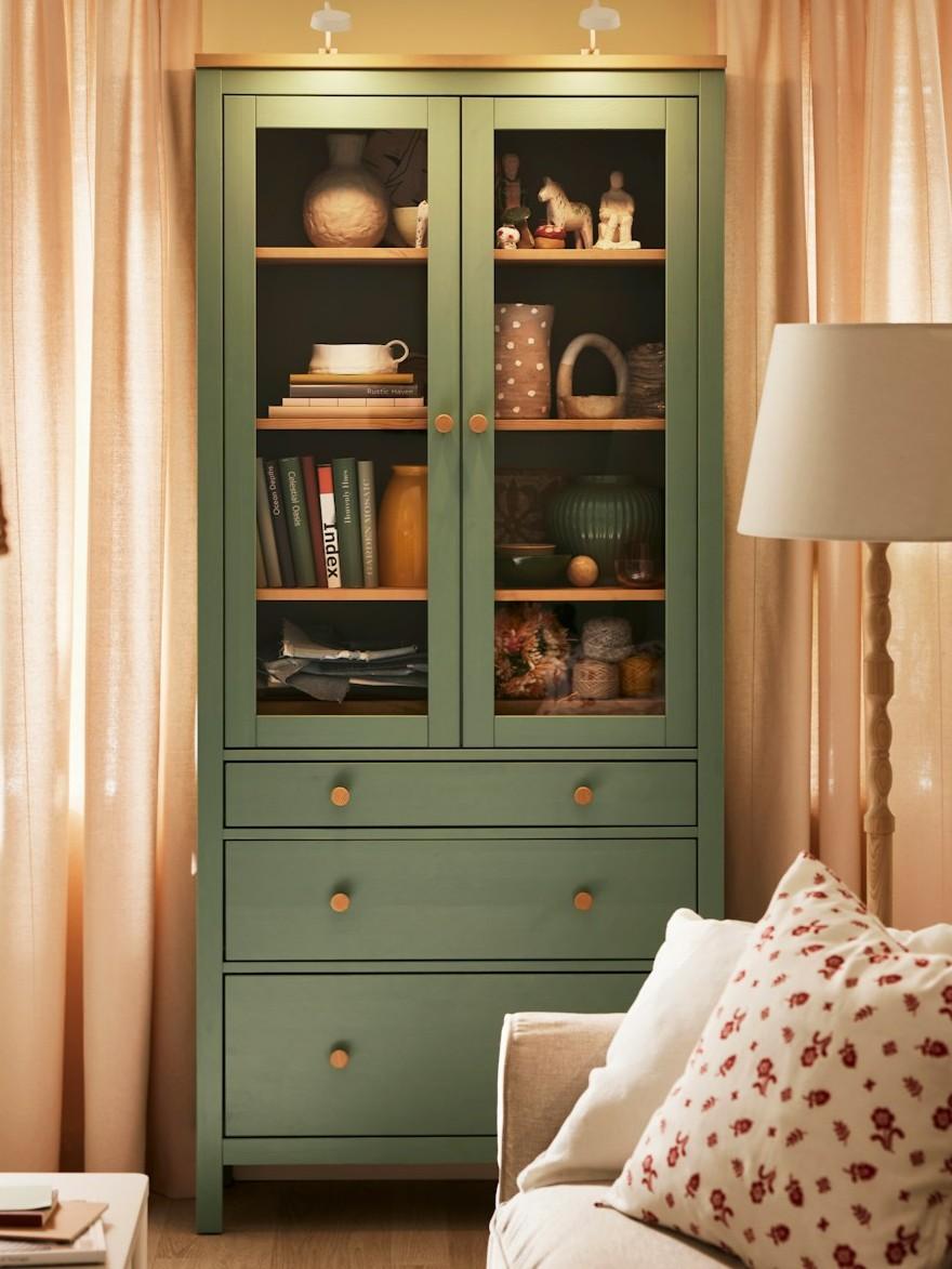 Zielona witryna HEMNES stojąca w jasnym pokoju dziennym.