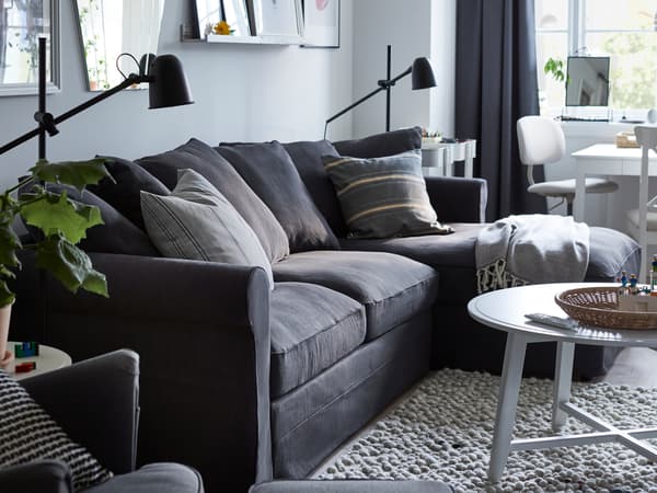 Zimmer mit einem GRÖNLID Bettsofa mit Récamiere, zwei SKURUP Stand-/Leseleuchten in Schwarz und verschiedenen Gemälden an der Wand.