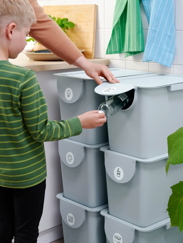 Zöld pulóvert viselő fiú a PET-palackot dob egy tetővel ellátott TRÖSKNING tárolóba.