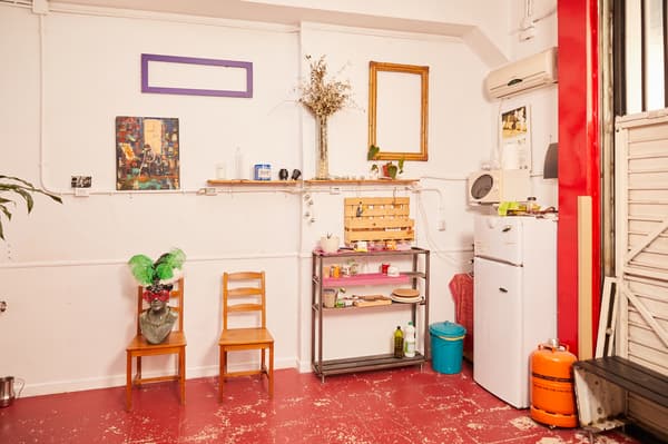 Zona amb nevera, microones, bombona de butà, prestatgeria amb utensilis de cuina, cadires i elements de decoració.