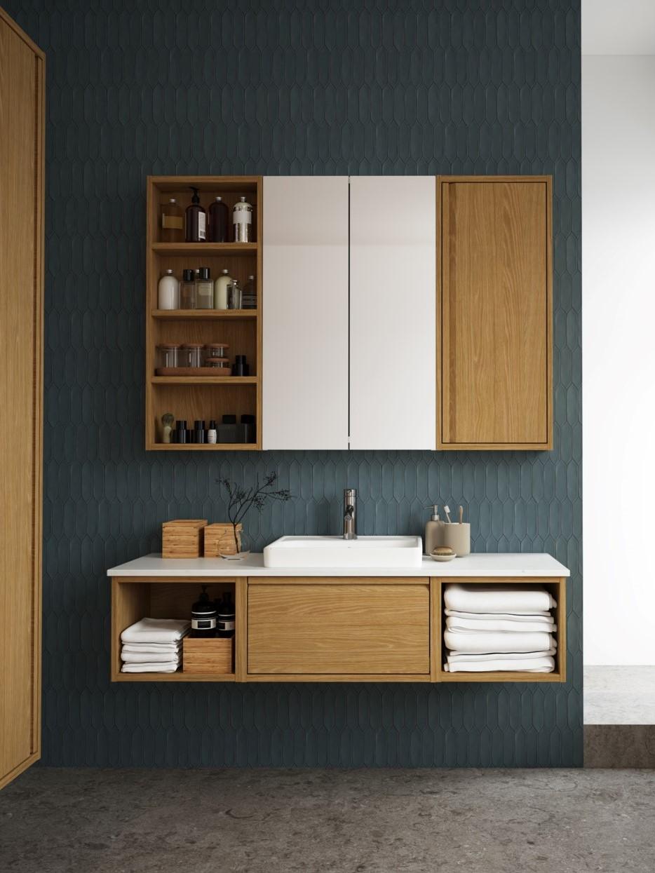 Zona bagno con mobile lavabo effetto legno e piano bianco con mobile a parete frontale legno e bianco. all'interno alcuni accessori per il bagno.