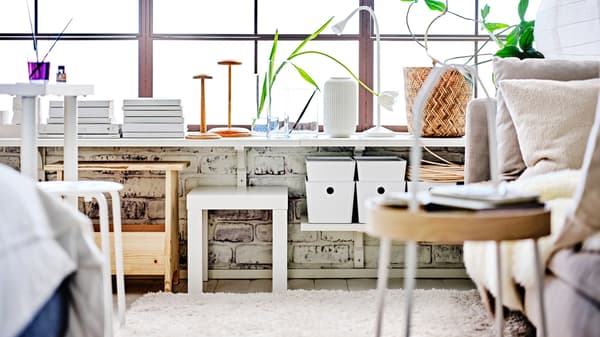 Zona de estar com estantes de parede BERGSHULT/RAMSHULT em branco com caixas com tampa KUGGIS em branco e mesa de apoio LACK em branco.