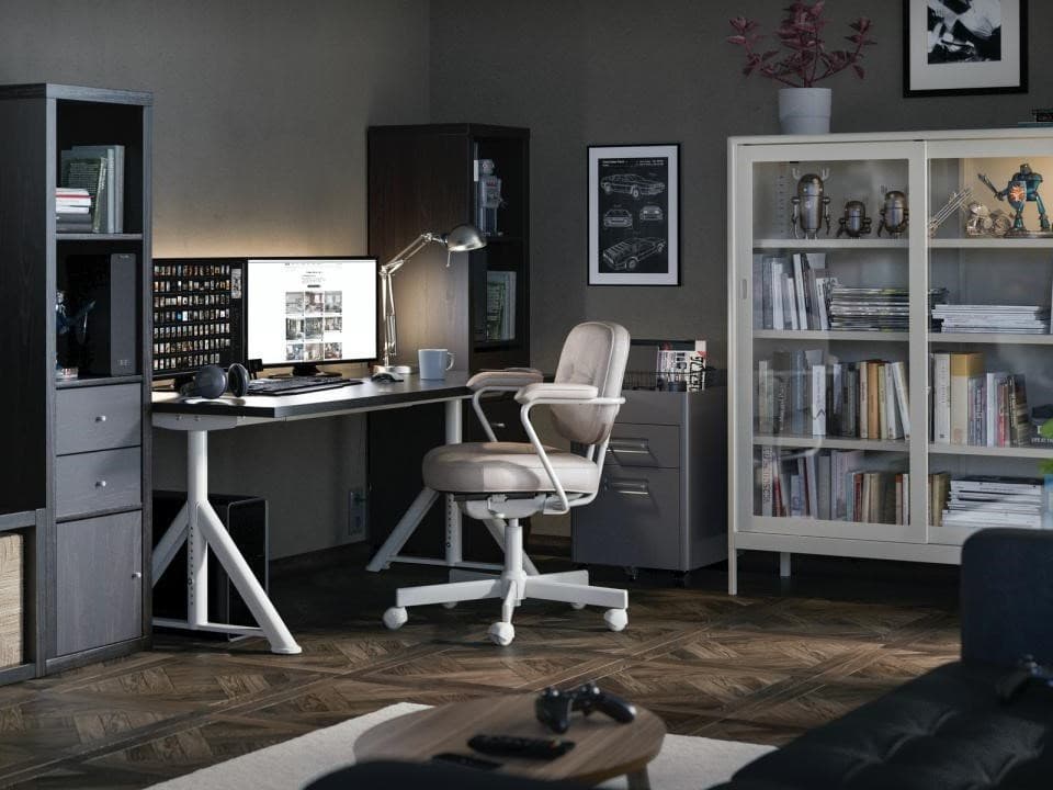 Zona de joc i treball amb escriptori blanc, cadira ergonòmica beix i prestatgeries plenes de llibres i figures. Decoració moderna i funcional amb inspiració gaming.