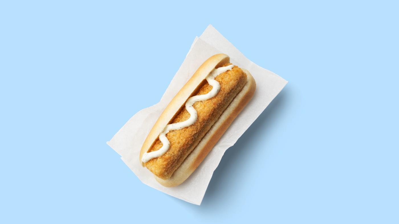 zu sehen ist ein Hot Dog Brötchen, darin ein Fischstäbchen mit Sauce Tartar. Auf hellblauem Hintergrund