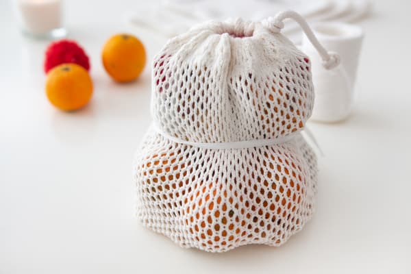 Zu sehen ist ein weißes Stoffsäckchen, in dem Mandarinen sind.