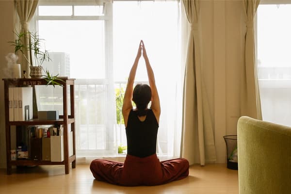 Zur neuen IKEA Studie: Eine Frau sitzt im Yoga-Sitz vor einem Fenster und blickt nach draußen.