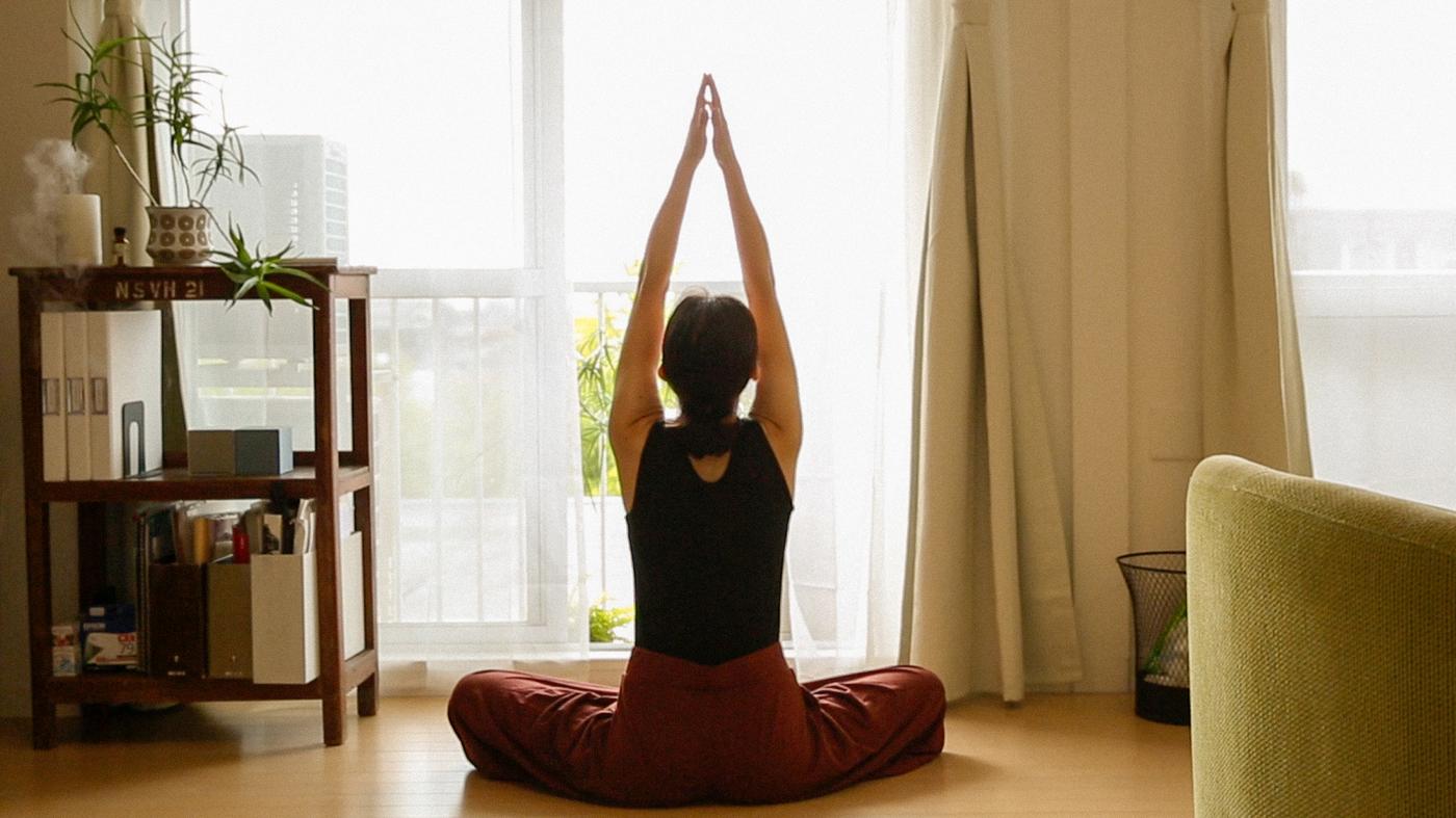 Zur neuen IKEA Studie: Eine Frau sitzt im Yoga-Sitz vor einem Fenster und blickt nach draußen.
