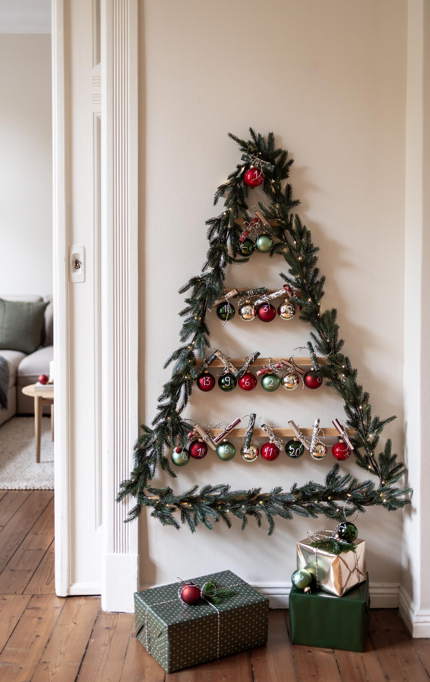 Zusammen mit Kindern wurde ein Adventskalender mit Gutscheinen in Form eines Tannenbaums gebastelt. Dieser hängt mit bunten Kugeln ein einer weißen Wand.