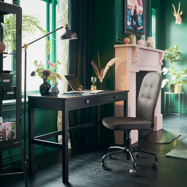 Zwartbruin HEMNES bureau staat bij het venster in een woonkamer met groene wanden en een roze haard