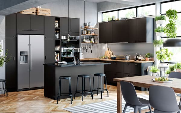 Zwarte IKEA KUNGSBACKA keukenkastdeuren en ladefronten gemaakt van gerecycleerde petflessen, plus zwarte barkrukken in een open keuken met luchtige aanblik.