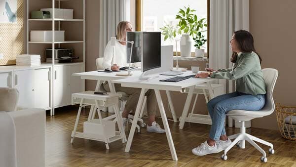 Zwei Frauen arbeiten an zwei weissen Schreibtischen in einem hellen Büro