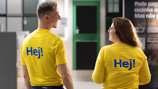 Zwei IKEA Mitarbeitende in gelber IKEA Oberbekleidung mit dem Wort „Hej“ auf dem Rücken stehen nebeneinander.