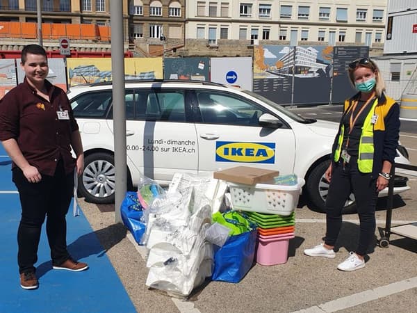 Zwei Ikea-Mitarbeitende stehen vor einem Auto und zeigen ihre Spenden