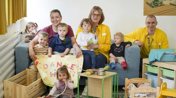 Zwei IKEA Mitarbeitende und eine Frau sitzen mit 6 Kindern zusammen.