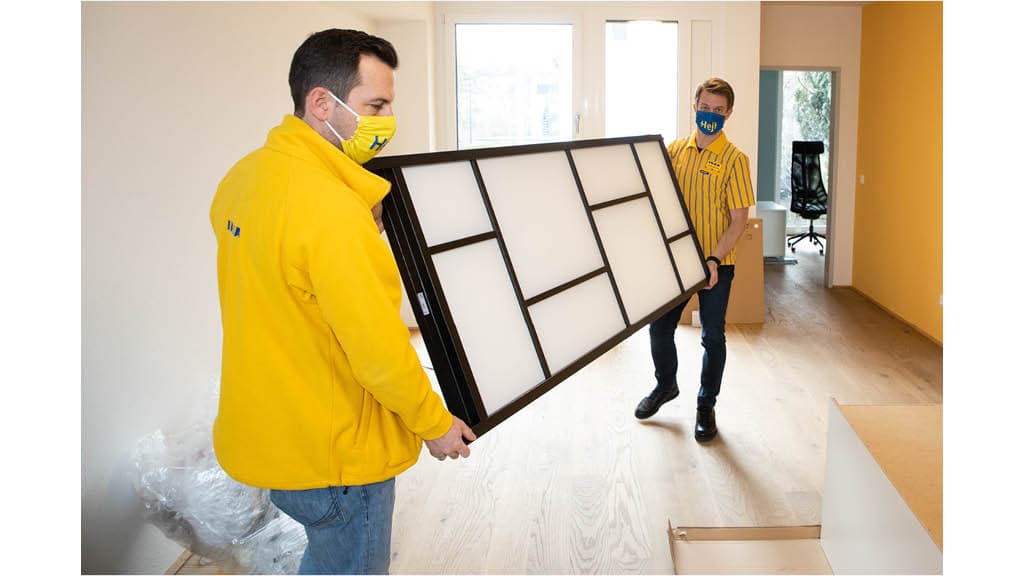 Zwei IKEA Mitarbeiter, die ein Möbelstück mit ihren Händen tragen.