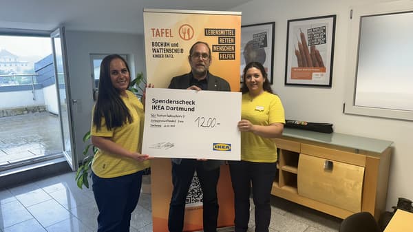 Zwei IKEA-Mitarbeiterinnen in gelben Shirts überreichen gemeinsam mit einem Mann einen Spendenscheck über 1'200 Euro an die Tafel Bochum Wattenscheid. Sie stehen in einem Büro mit Informationspostern zur Lebensmittelrettung.