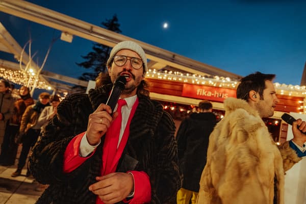 Zwei in Anzuügen gekleidete Männer singen auf einem Weihnachtsmark