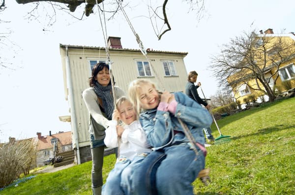 Zwei Kinder sitzen auf einer Schaukel zusammen und werden von einer Person angeschubst.