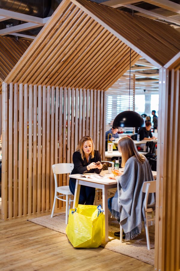 Zwei Kundinnen sitzen gemeinsam in einem Holzhäuschen im IKEA Restaurant und essen ihr Essen.