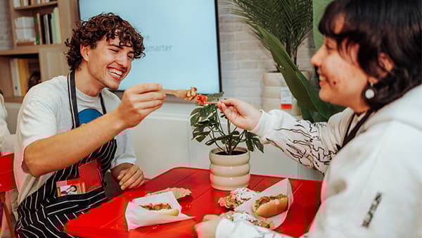 Zwei lächelnde Personen Hotdog essend auf einem roten Tisch