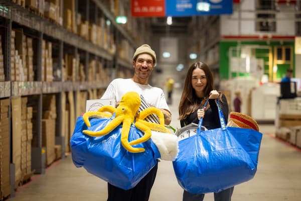 Zwei Personen halten zwei blaue FRAKTA Taschen hoch, die gefüllt sind mit IKEA Produkten.