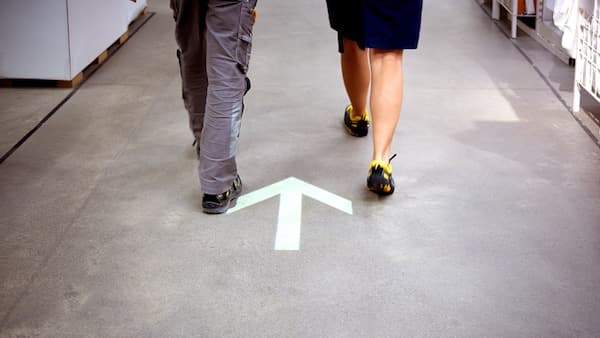 Zwei Personen laufen nebeneinander. Auf dem Boden ist ein Richtungspfeil.